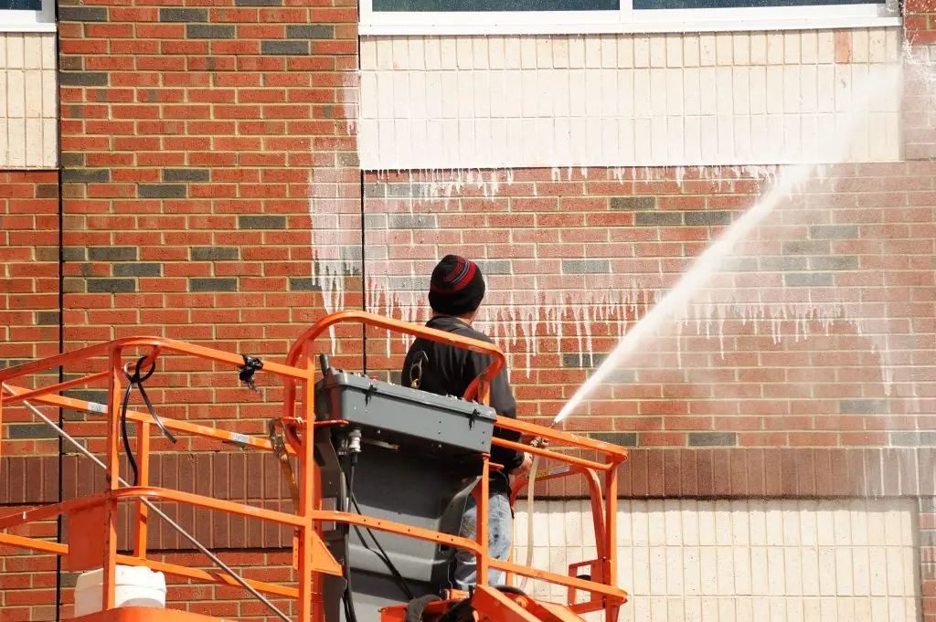 outdoor worker cleaning the exterior wall of building through pressure water - Packard Power Washing office building cleaning